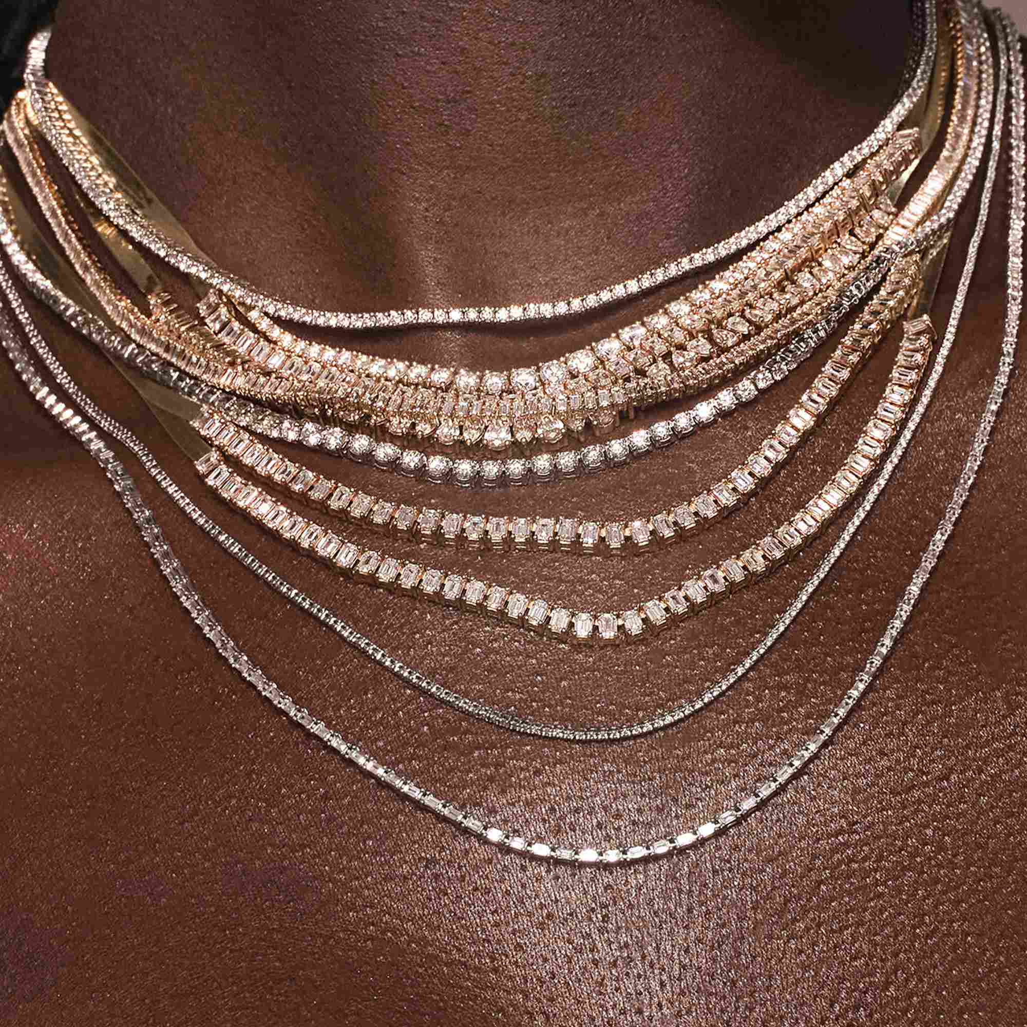 A close-up of layered metallic necklaces on dark skin.