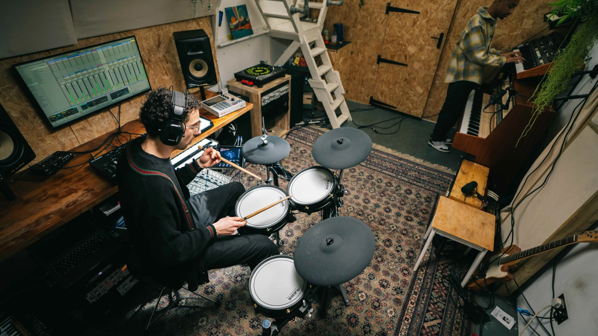 Person playing electronic drums in a cozy music studio setting.