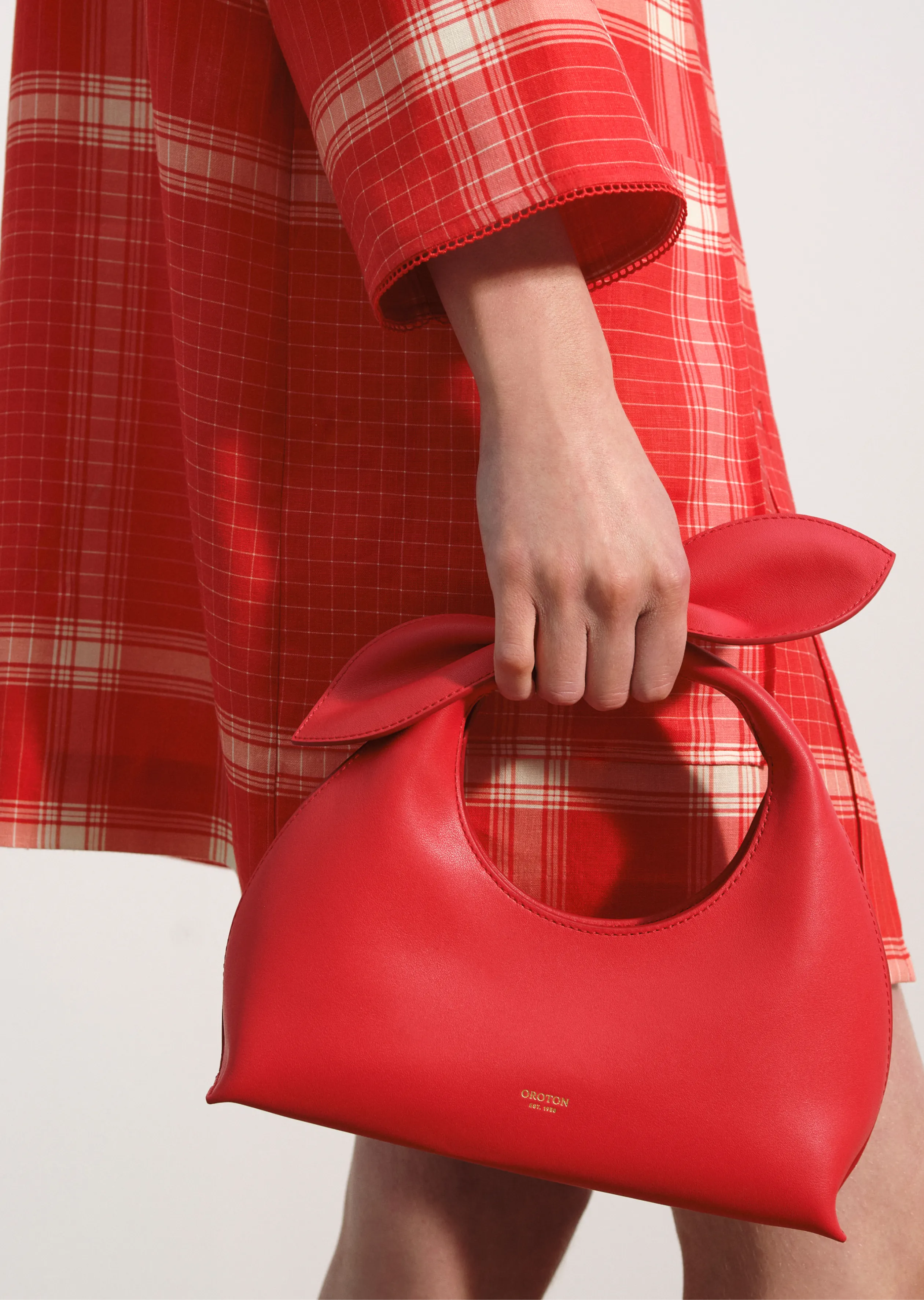 A person holding a red handbag while wearing a red plaid dress.