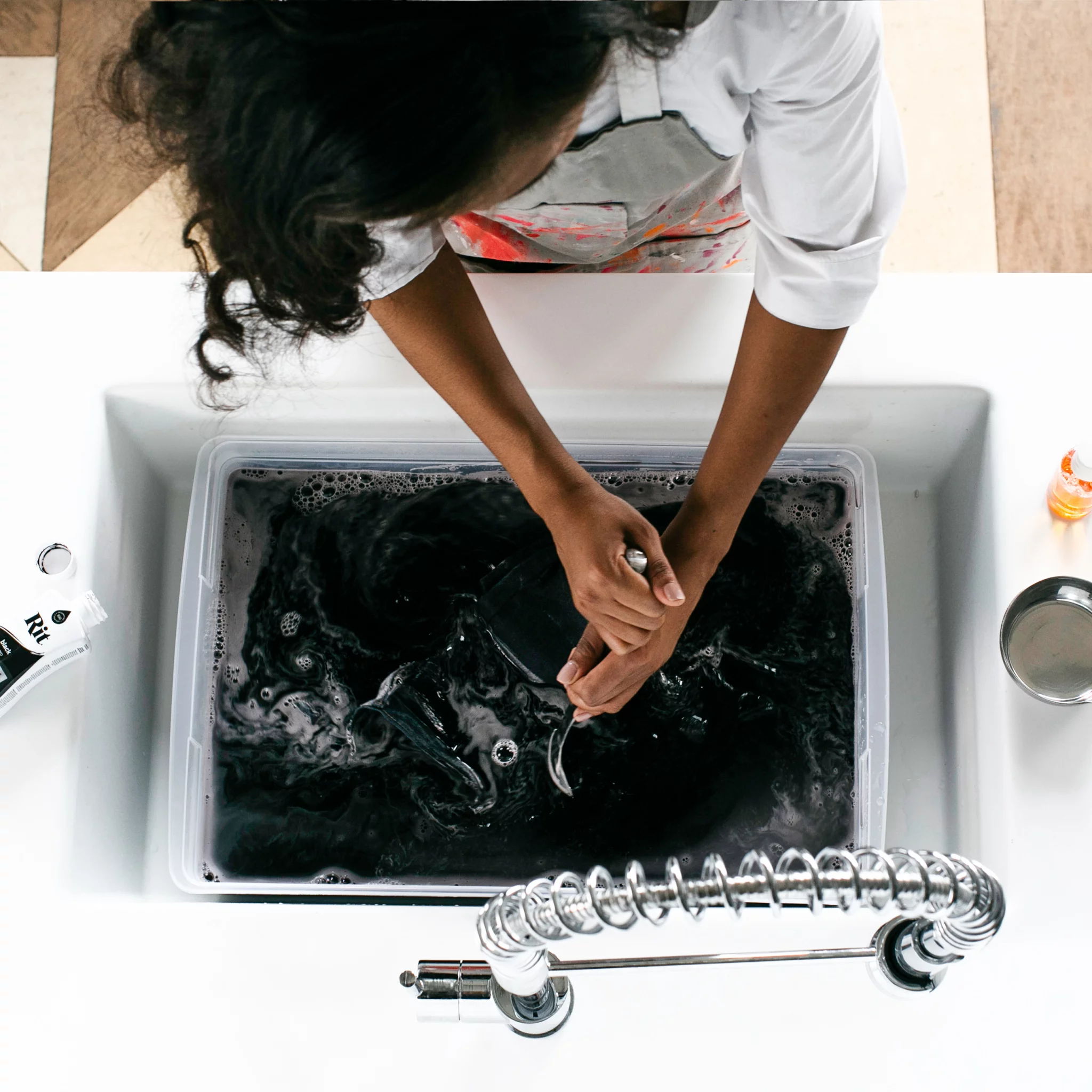 Person washing dark clothing in a sink with bubbles.
