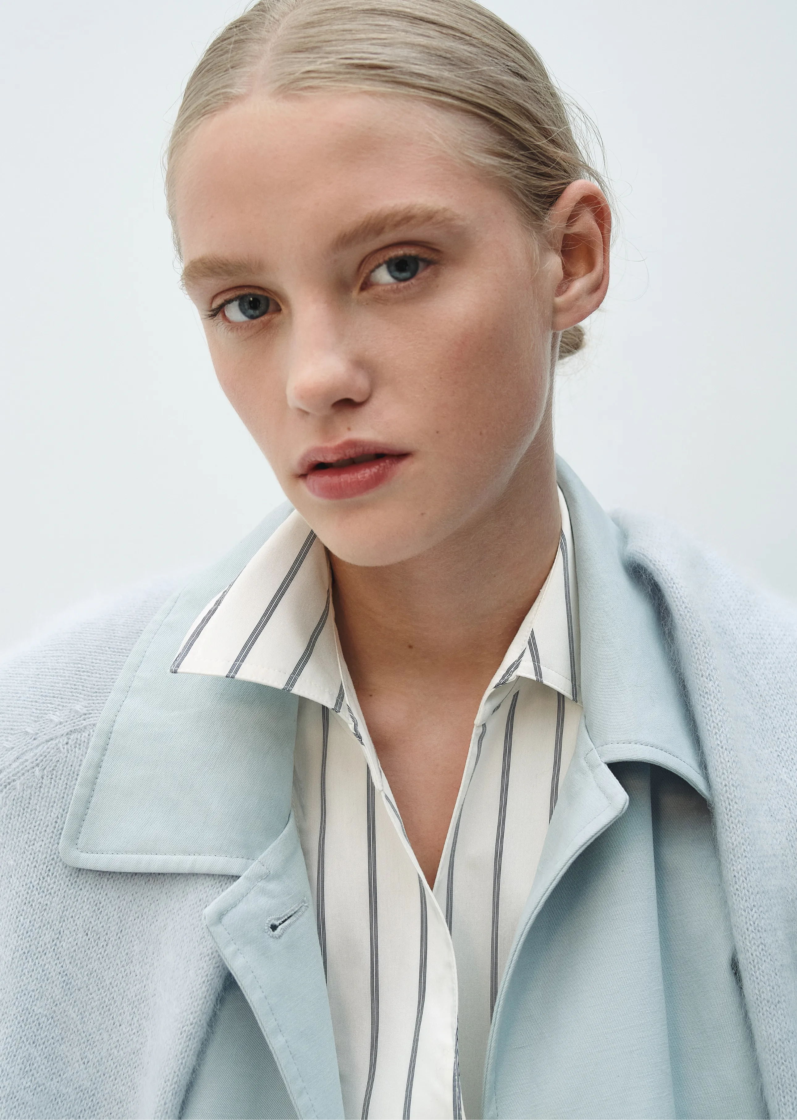 A young woman with blonde hair wearing a light blue jacket and striped shirt.