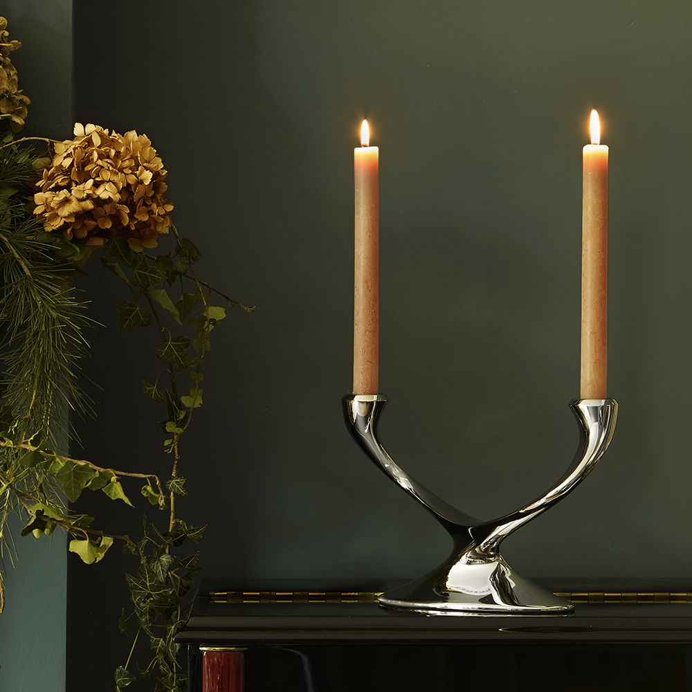 Two lit candles in a Windrush Candelabrum against a dark green background.