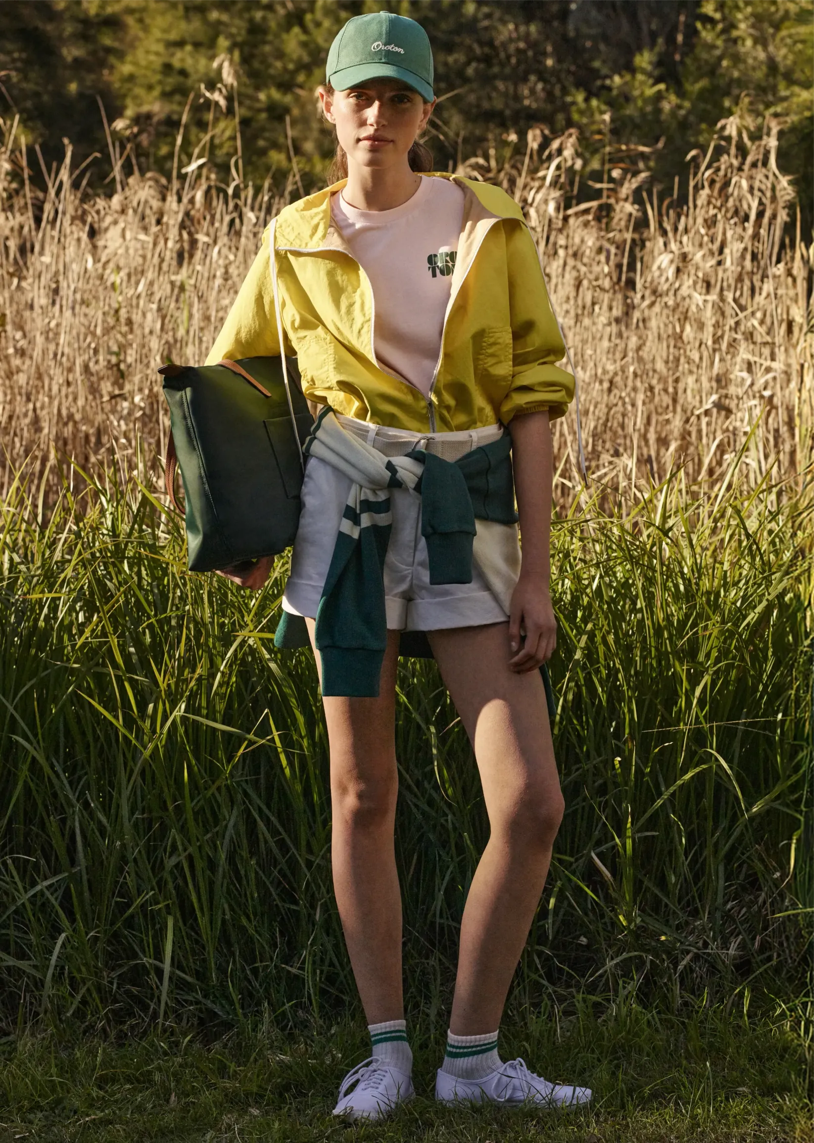 Person in yellow jacket and cap, standing in tall grass.