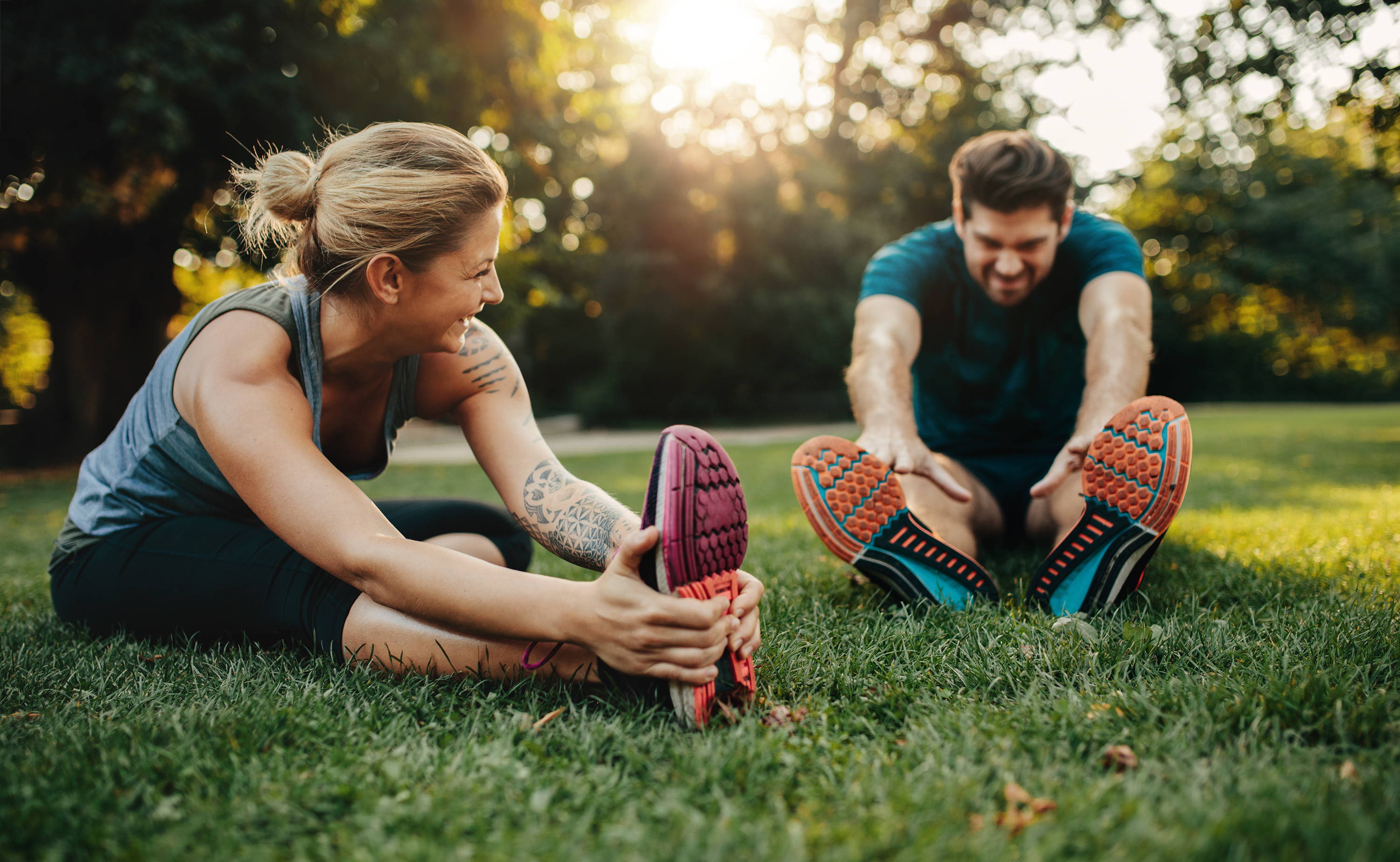 Post-Workout recovery. Woman and man stretching on grass.