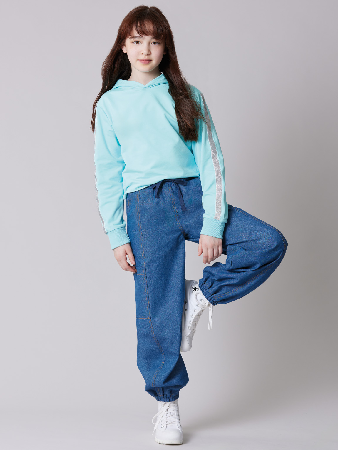 A person in a mint hoodie and blue pants standing on one leg.