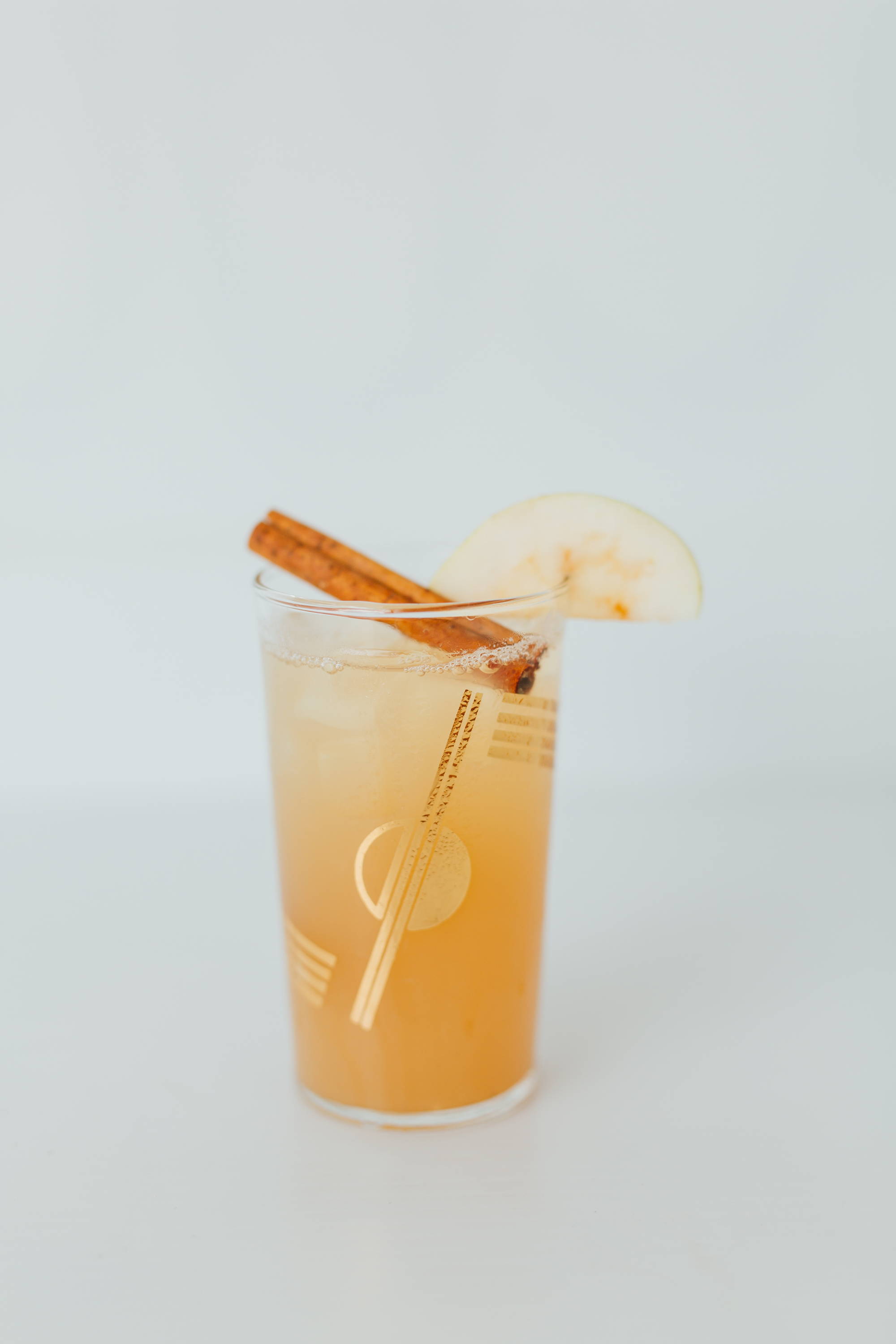 brown cocktail with an apple slice garnish, in a tall glass