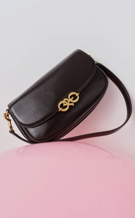 Black leather crossbody bag with a gold clasp on a pink surface.