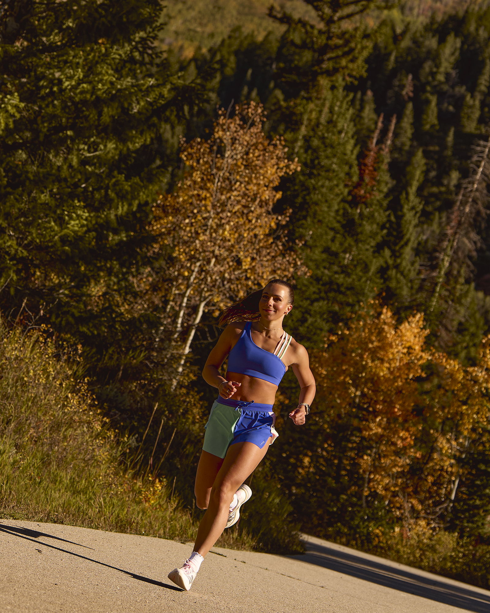 A woman running on a scenic road surrounded by autumn trees.