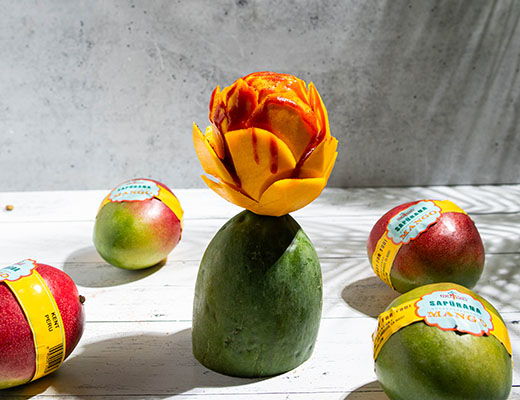 A carved mango flower on a green base with apples around it.