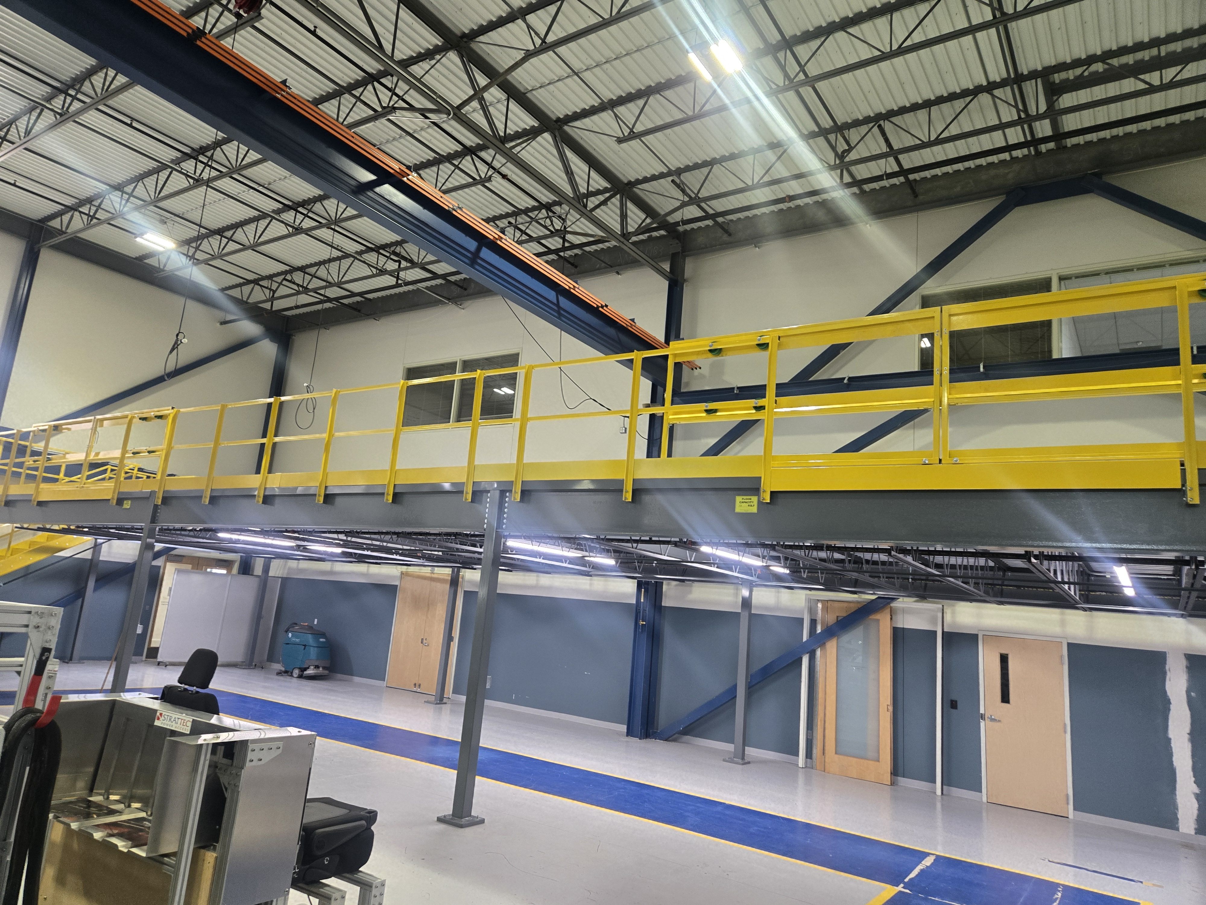 Interior of a warehouse with a yellow railing and overhead structure.