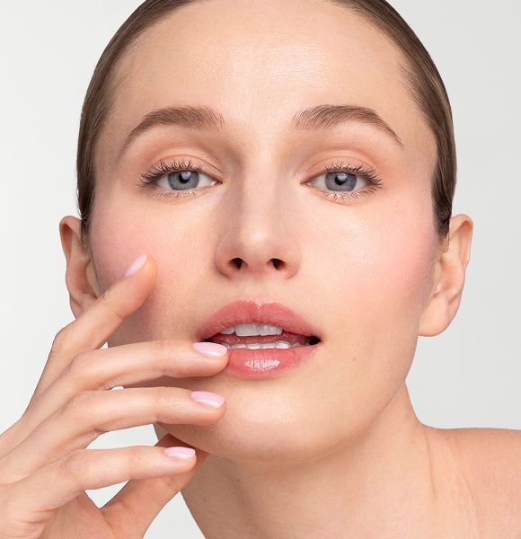 A woman with natural makeup gently touching her face, looking at the camera.