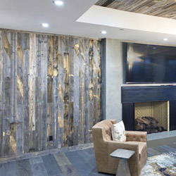Reclaimed wood wall in a room with a recessed reclaimed wood ceiling and a fireplace in a modern style room.