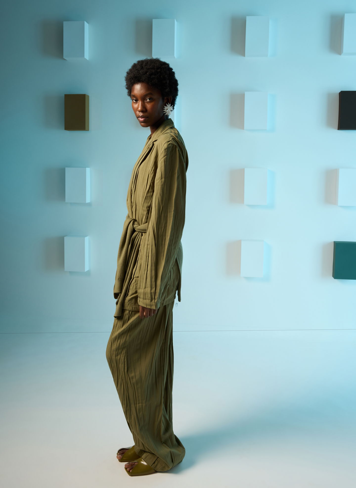 Model in olive green outfit against a minimalist background.