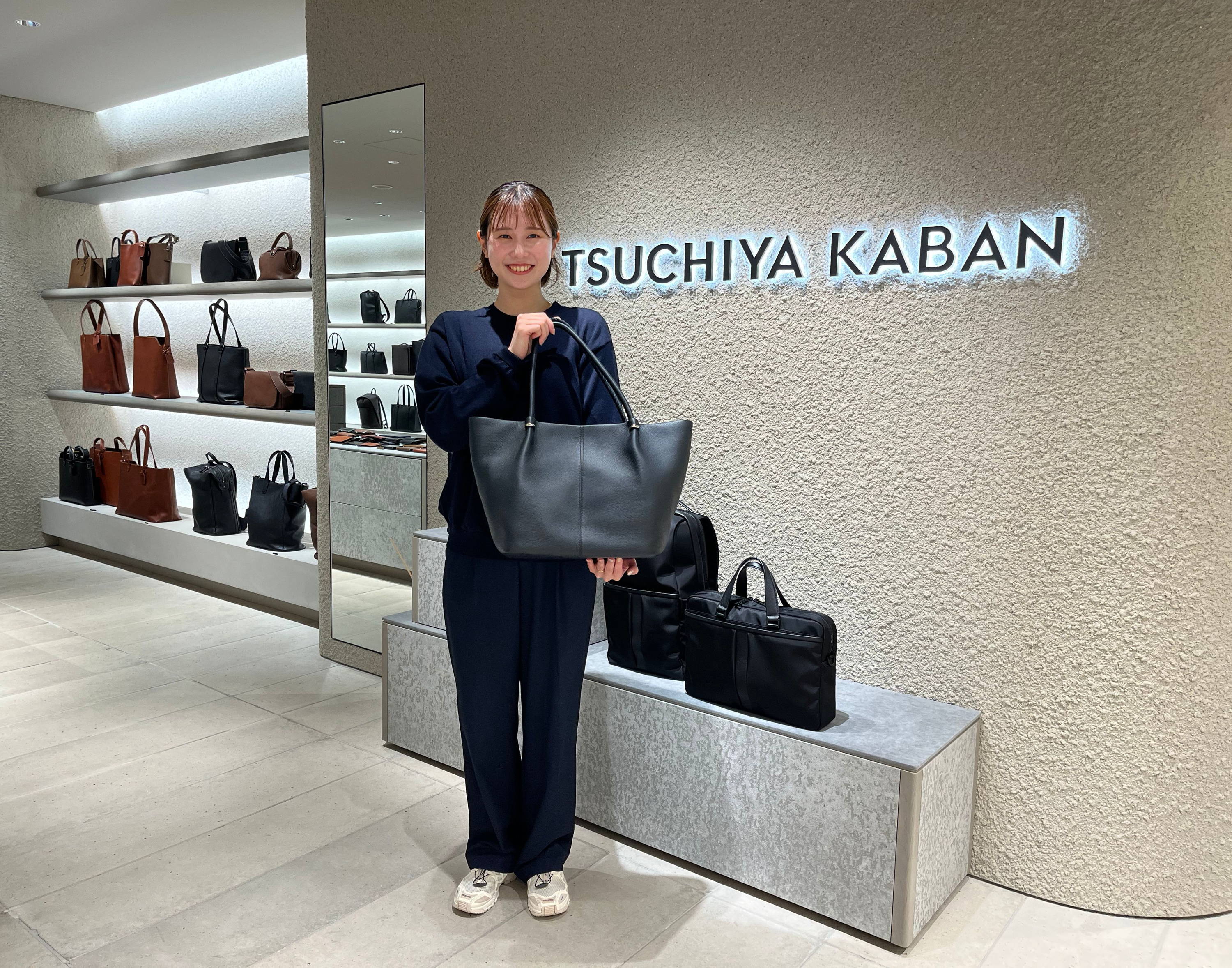 Person holding a black bag in a store displaying various bags.