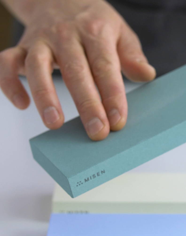 A chef rubbing the coarse surface of a green 220-grit Misen Sharpening Stone.