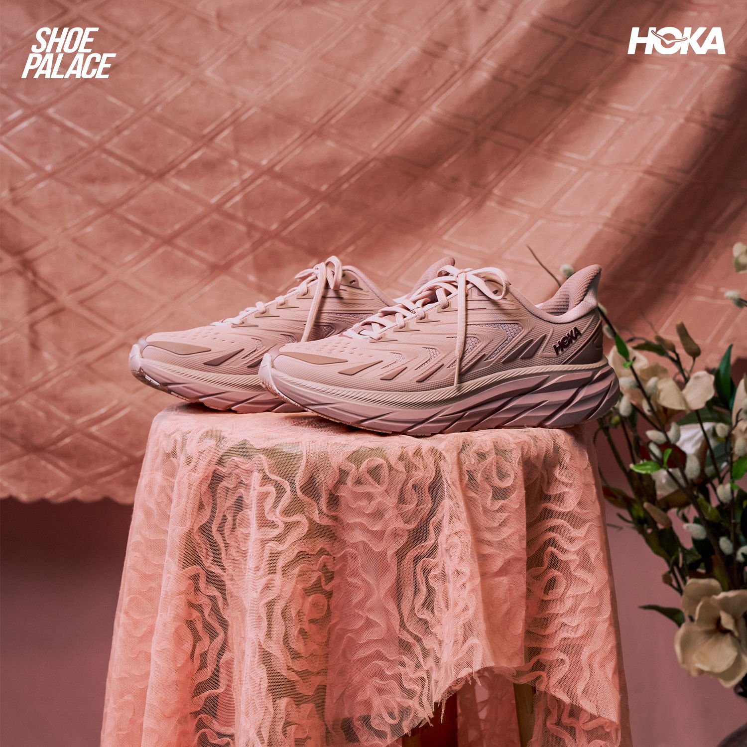 Pink sneakers displayed on a lace tablecloth with flowers in the background.