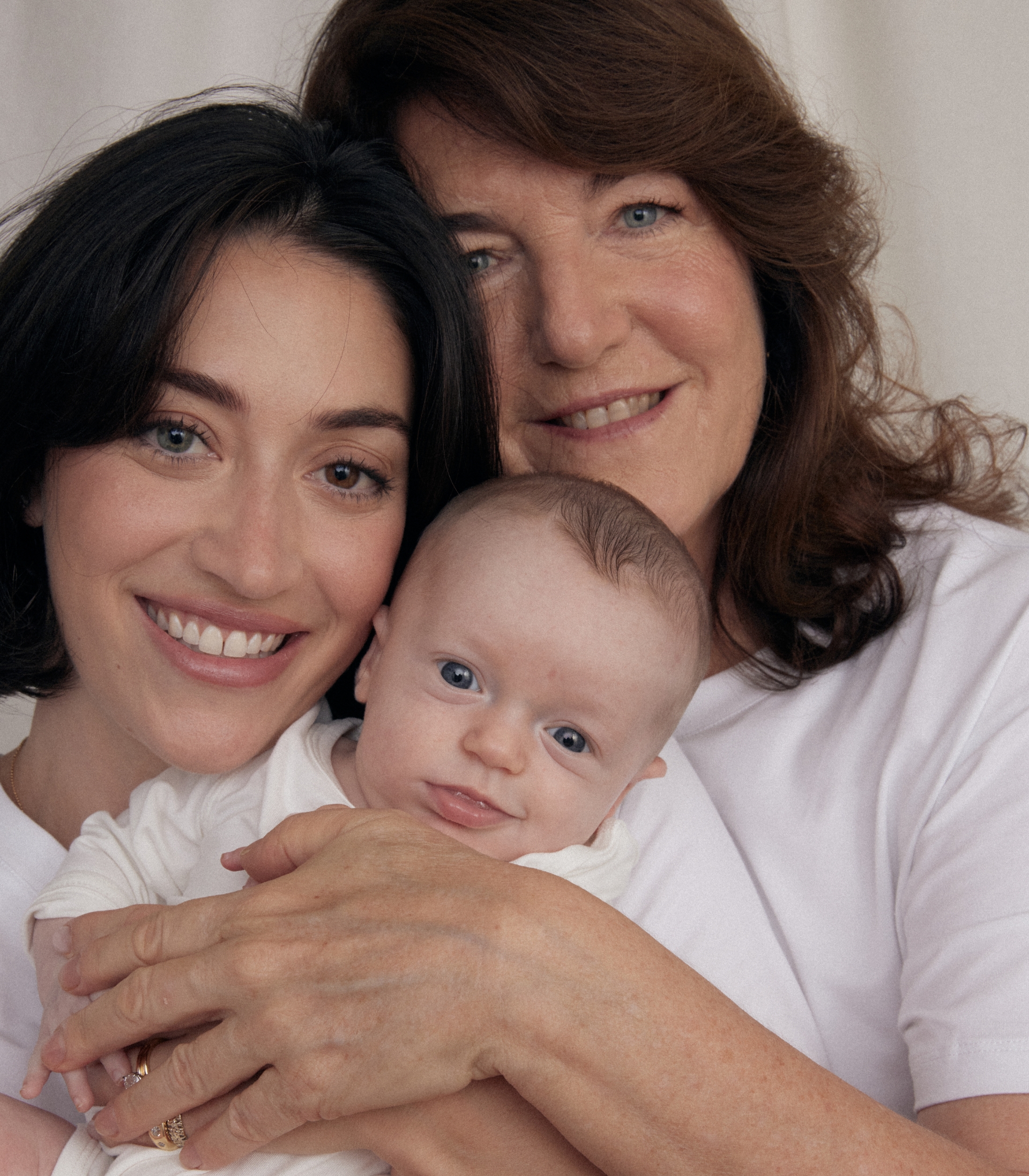 A mother, grandmother, and baby smiling together in a cozy setting.