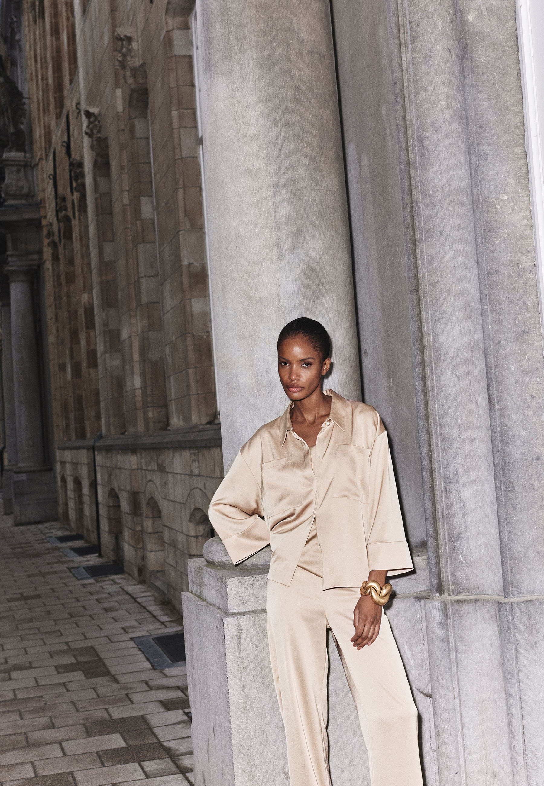 A person in beige clothing stands near a stone column.