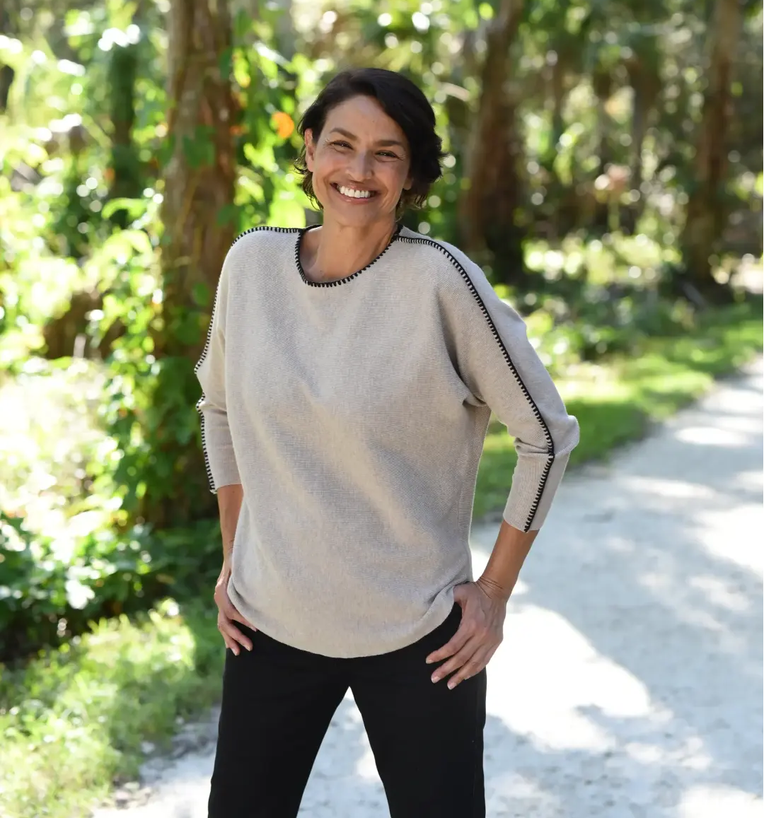 A smiling woman with short, dark hair stands on a footpath in a park. 