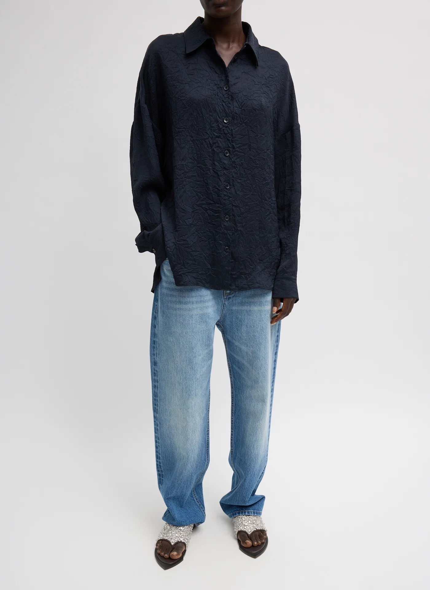 Person wearing a dark shirt and light blue jeans, standing on a gray background.