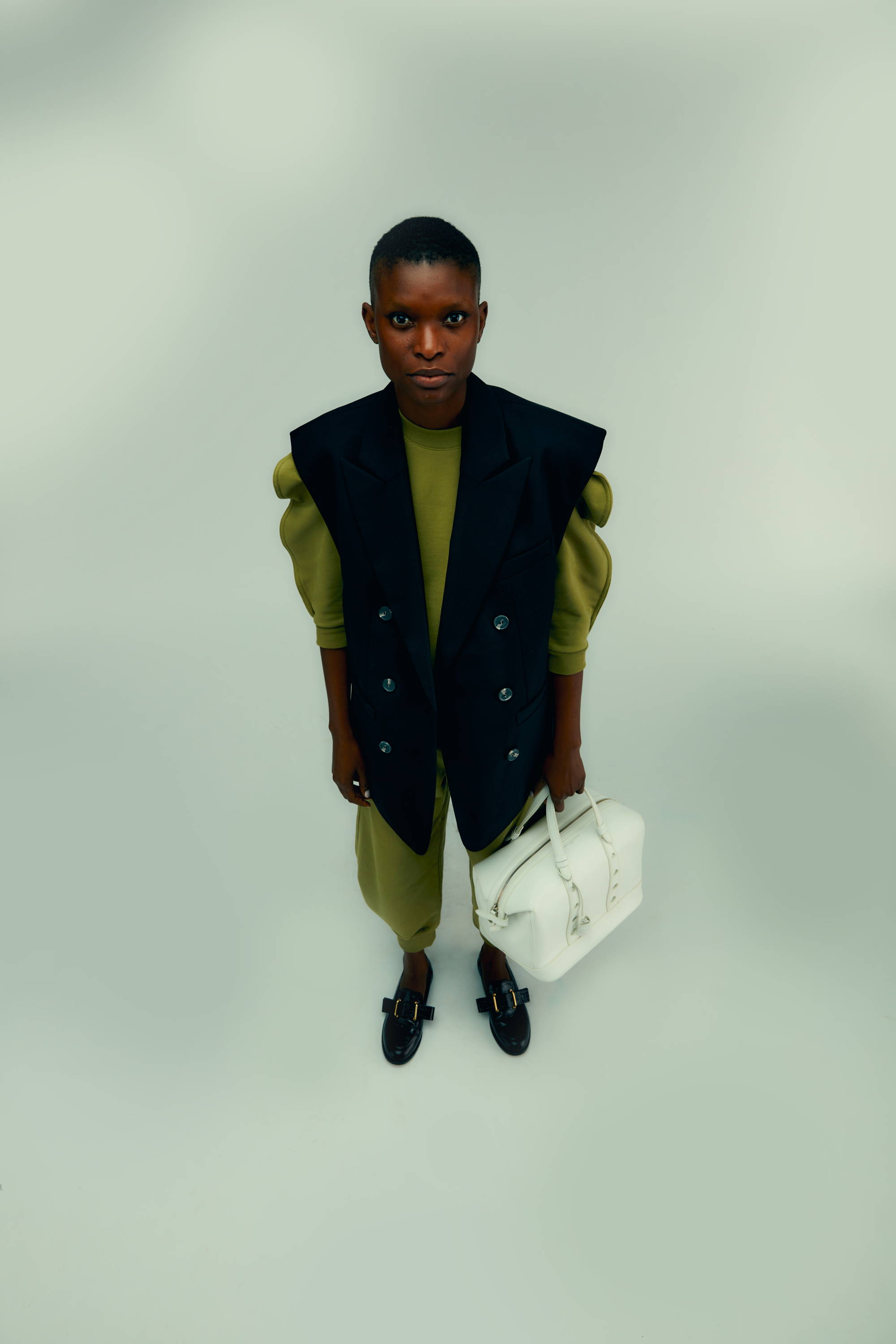 Person wearing a stylish outfit, holding a bag, standing against a neutral background.