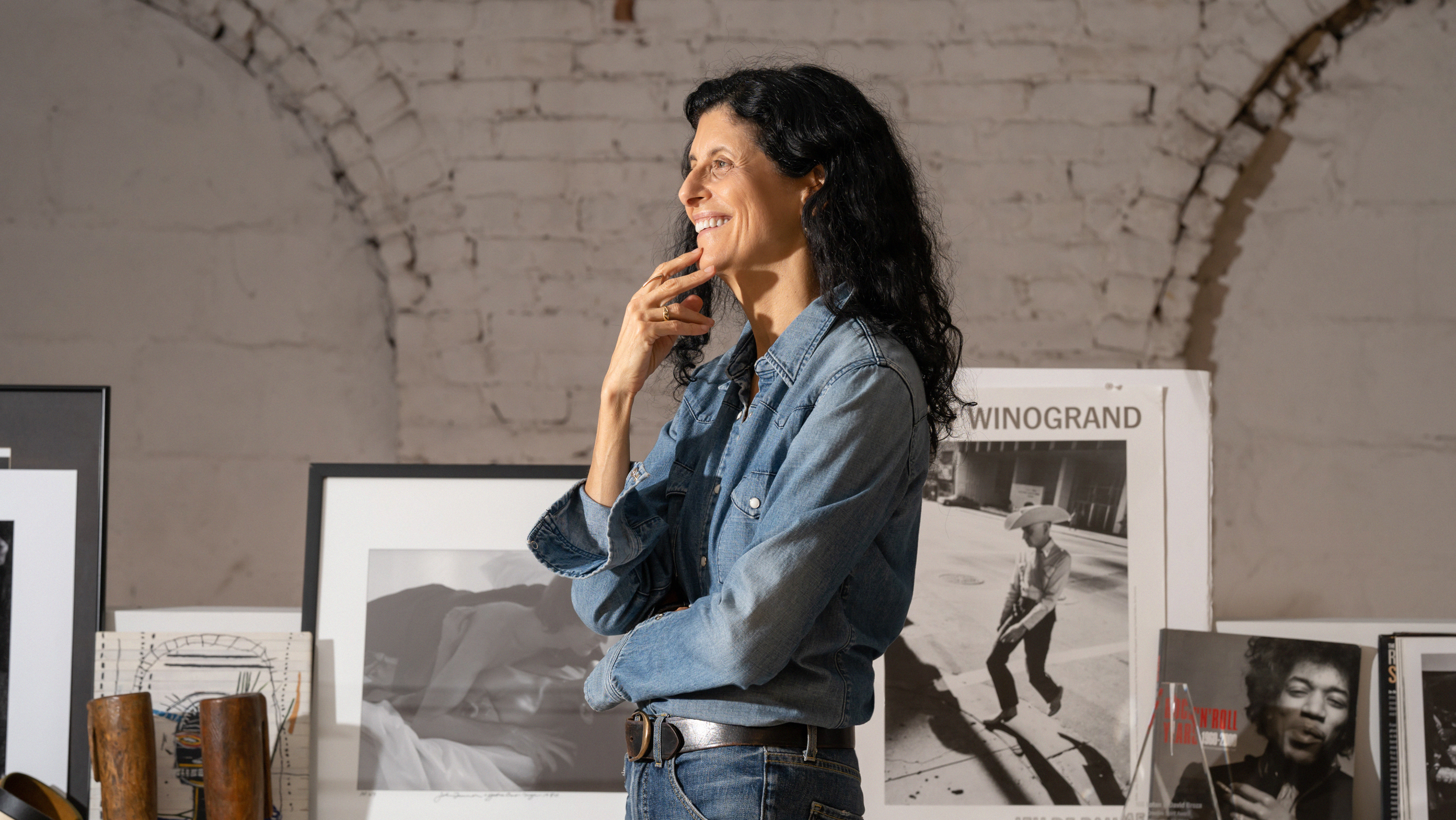 Woman in denim shirt thinking, surrounded by framed photographs in a gallery.
