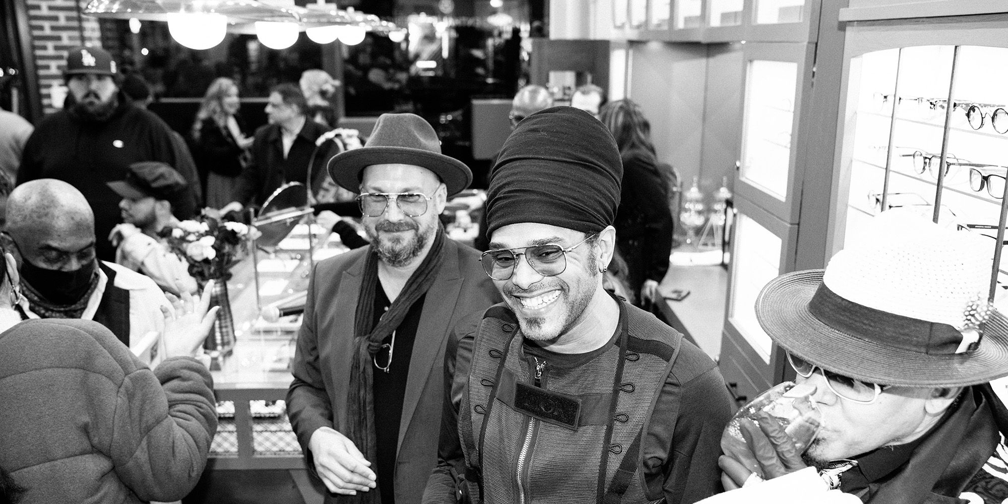 Two men smiling in a crowded market, wearing hats, in black and white.