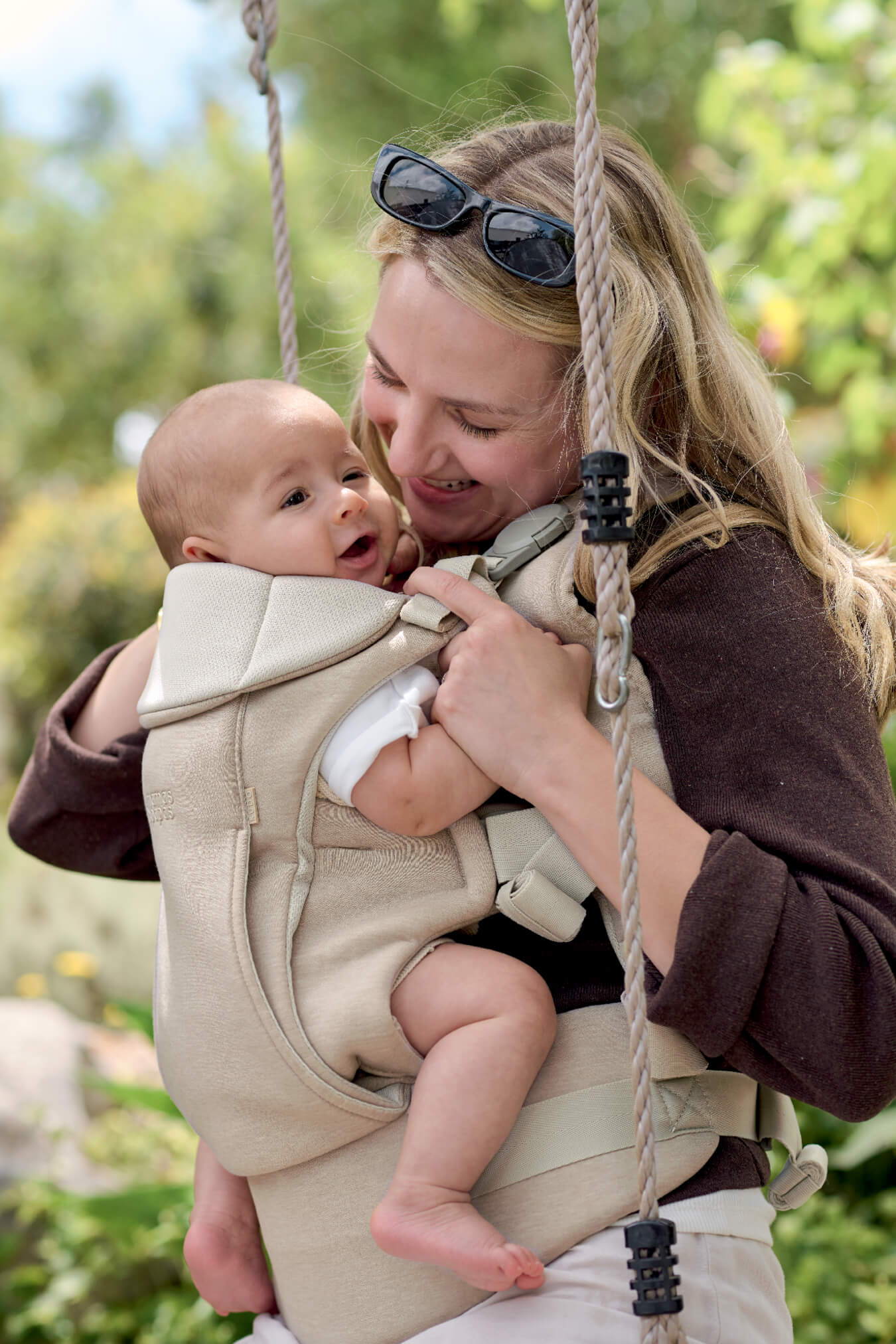 Mother holding a baby in a baby carrier on a swing.
