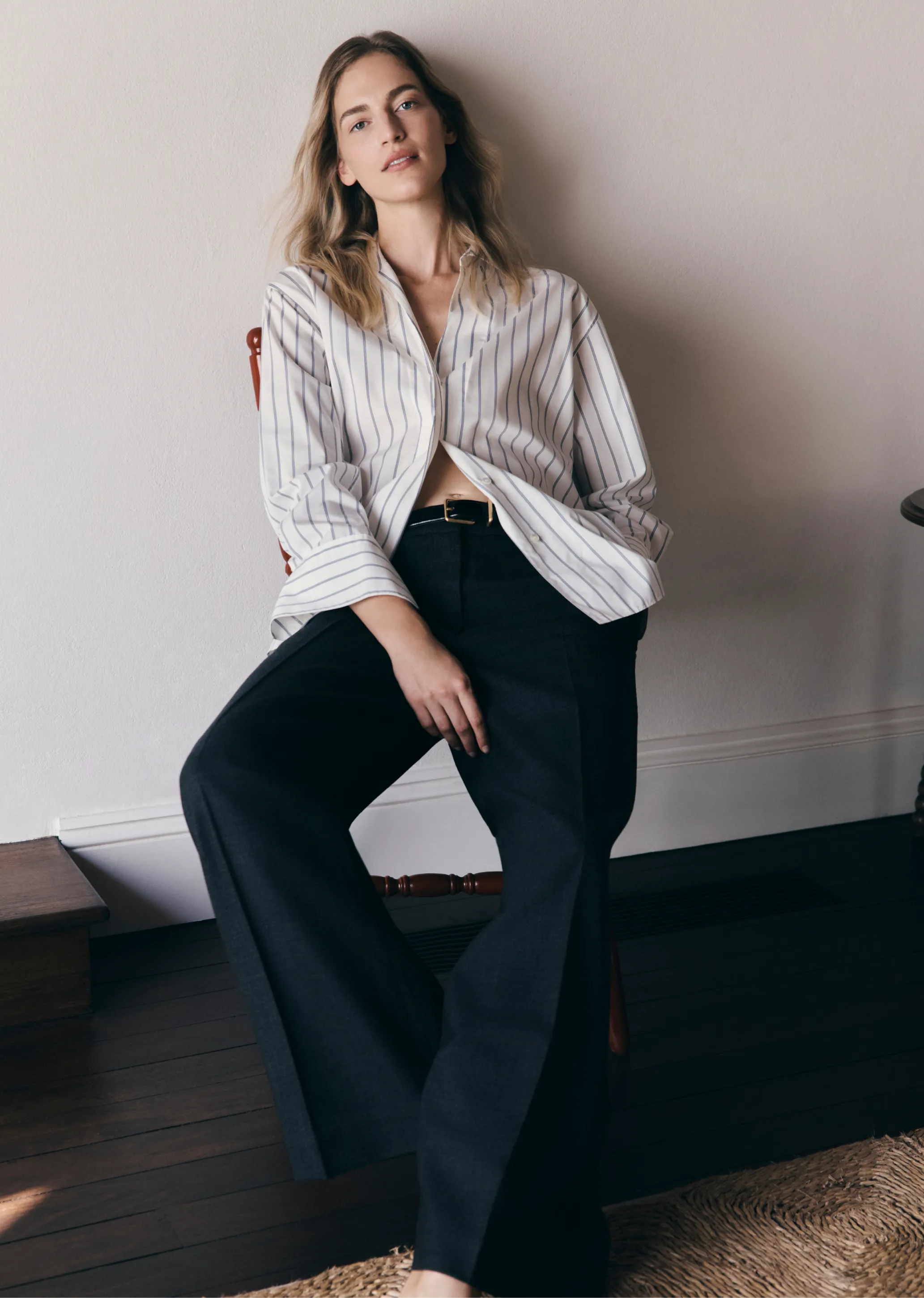 Woman in striped shirt and wide-leg pants sitting on a chair.