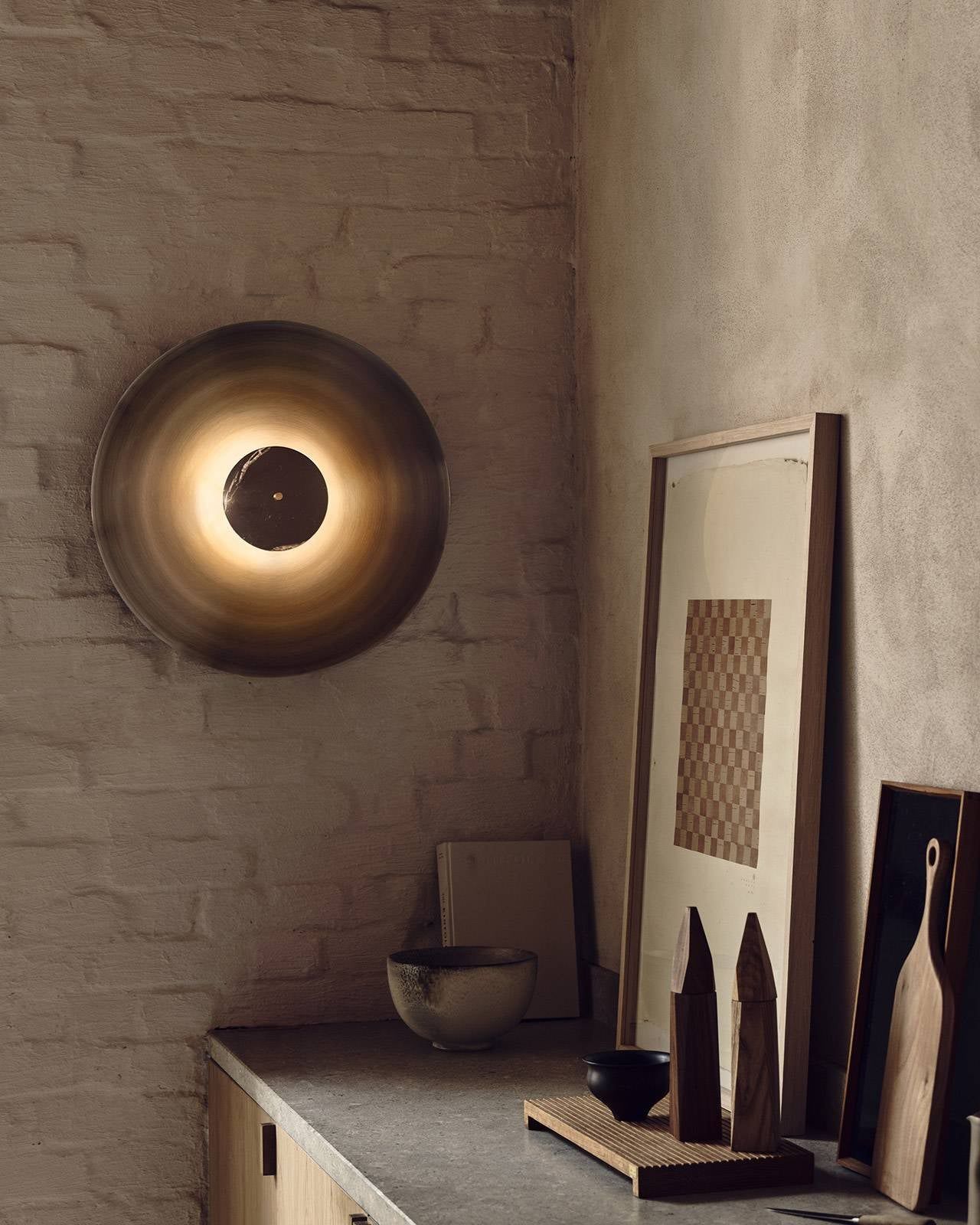 Decorative wall light fixture on a textured wall with framed art and wooden items below.