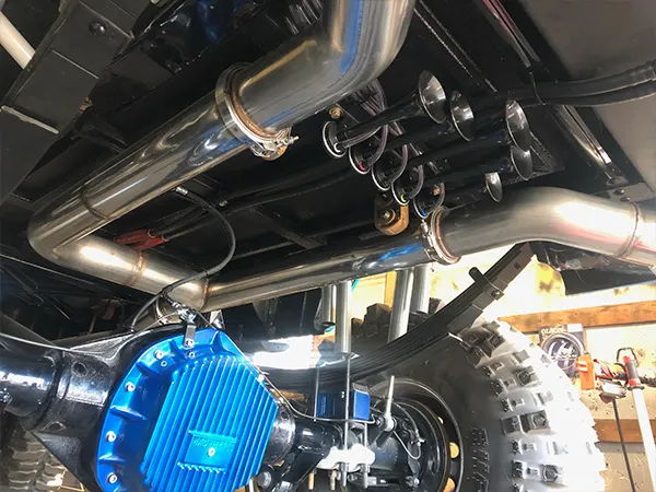 Close-up underside view of the black horn bells mounted beside the polished exhaust on the Linco Diesel Performance Suburban, install photo 4