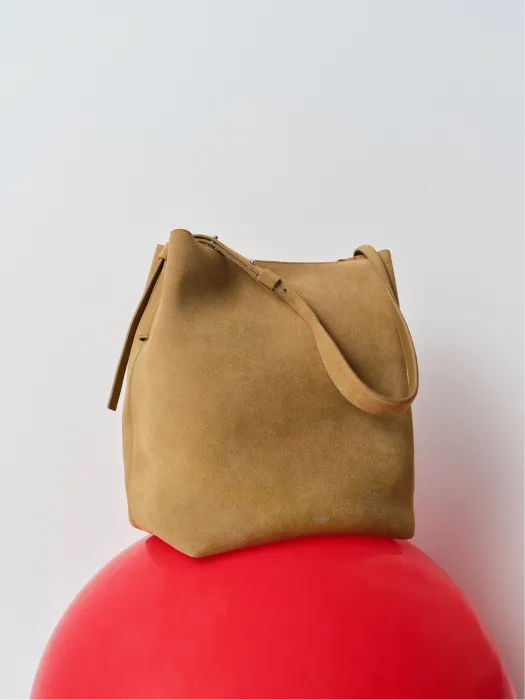 A brown suede bag resting on a red spherical surface.