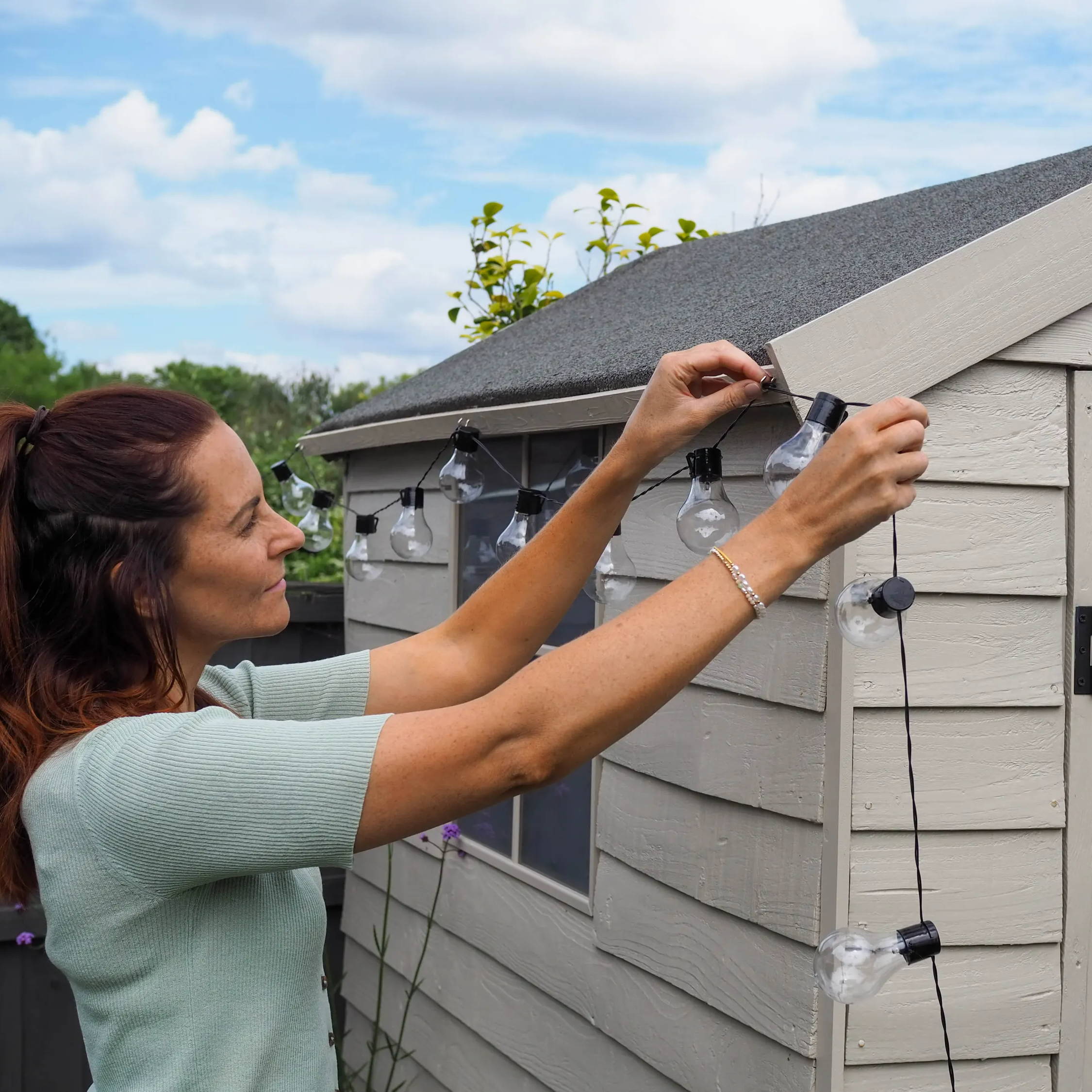Person hanging solar festoon lights on her garden shed.