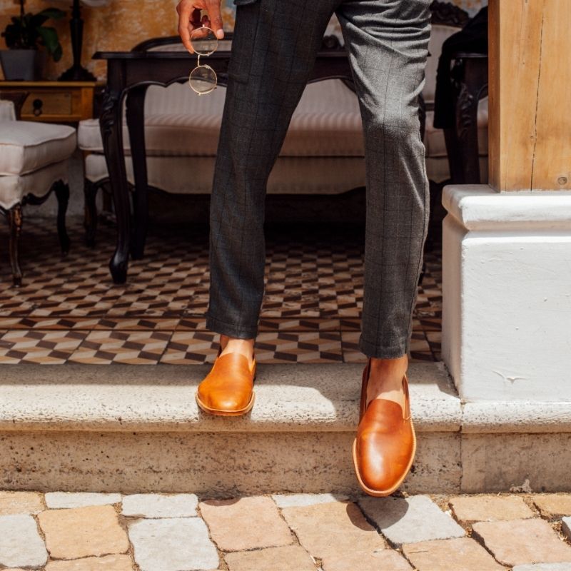 A man wearing tailored trousers and Adelante tan leather wide width dress loafers standing on a stone step.