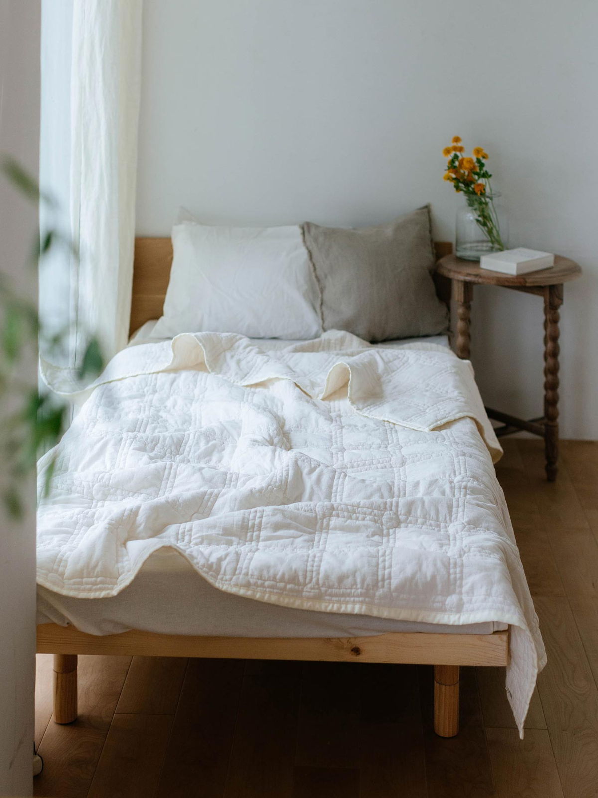 Cozy bed with white bedding and a vase of flowers on a side table.