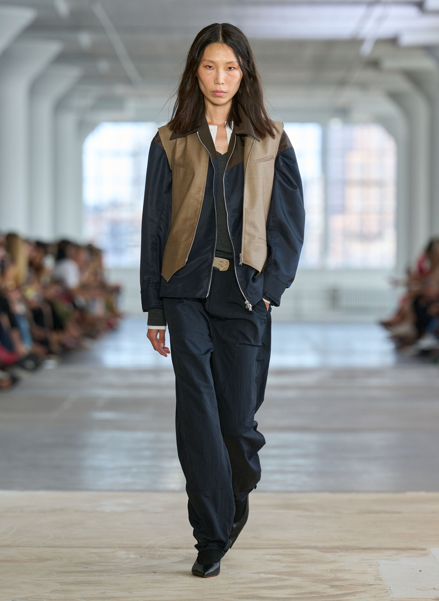 Model walking on runway in stylish outfit during fashion show.