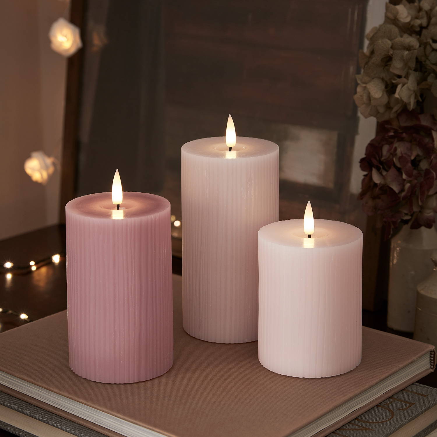 3 blush pink LED candles on a side table at night.