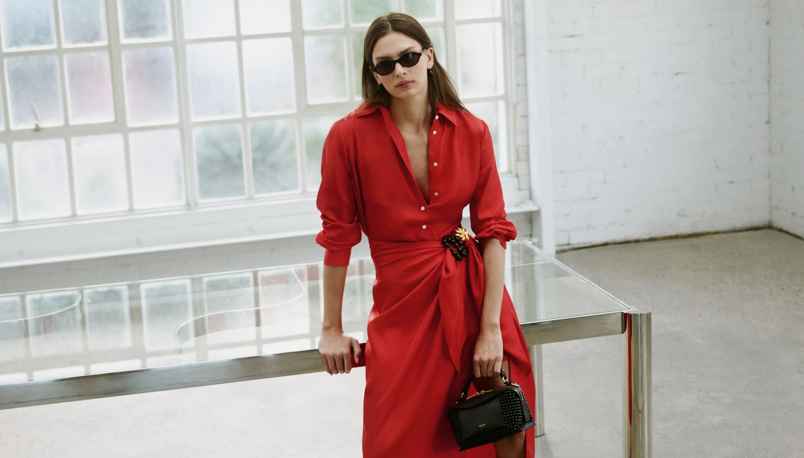 Woman in a red dress and sunglasses, standing in a bright room.