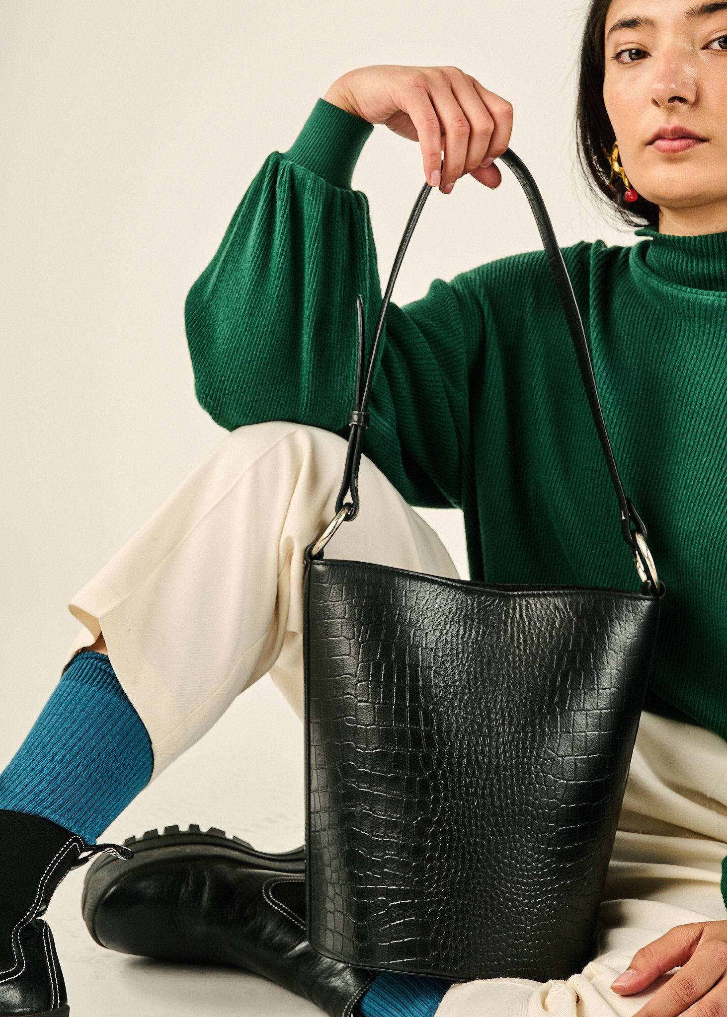 a girl sits holding a black croc bucket bag on her lap