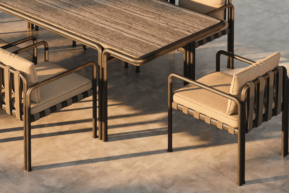 Close-up of an outdoor dining set with a rectangular table and cushioned lounge-style dining chairs in a warm neutral frame on a concrete patio.