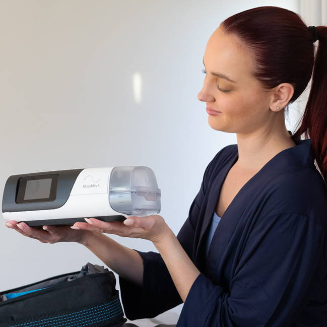 Woman holding a CPAP device in a room with a gray bag.