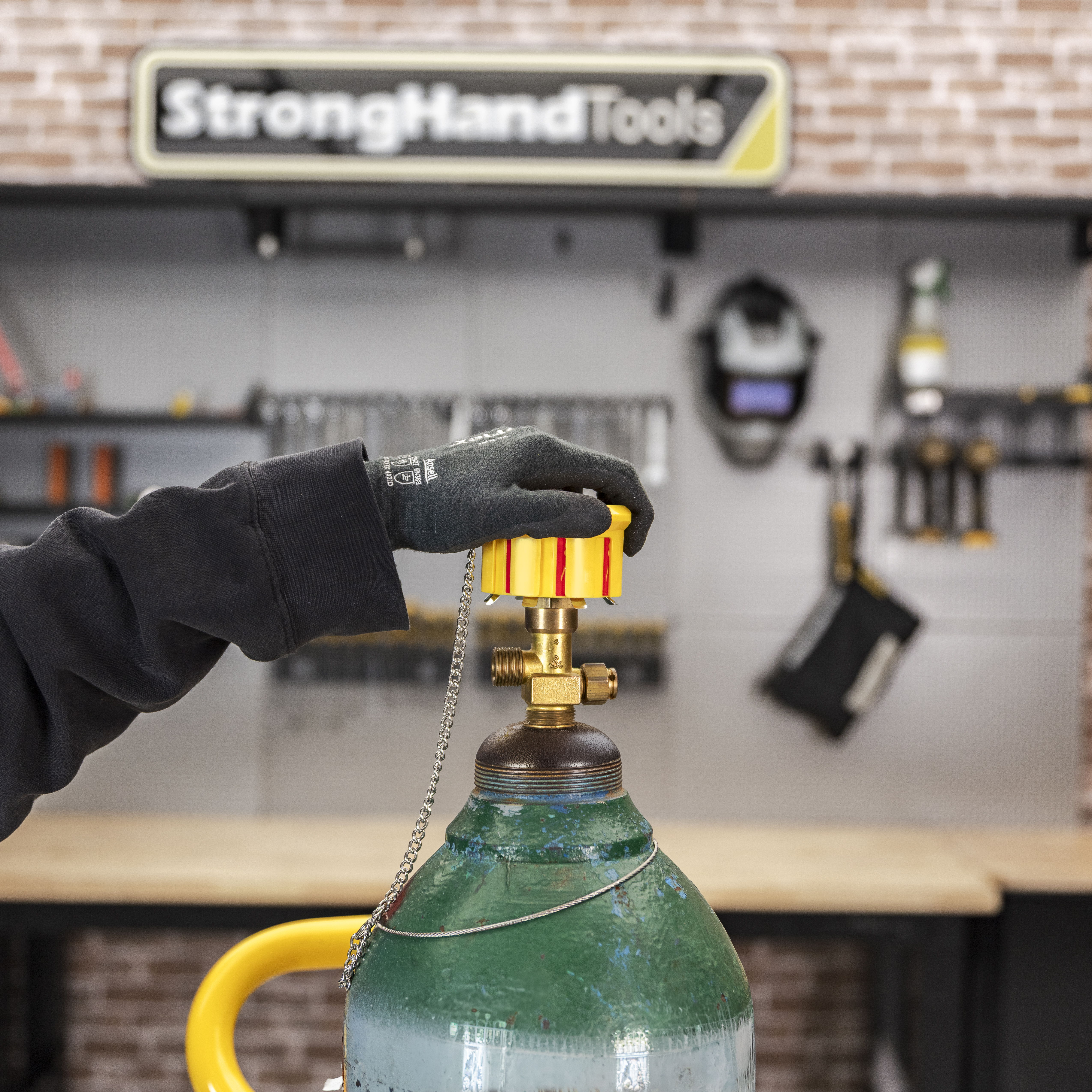 Hand adjusting a valve on a gas cylinder in a workshop setting.