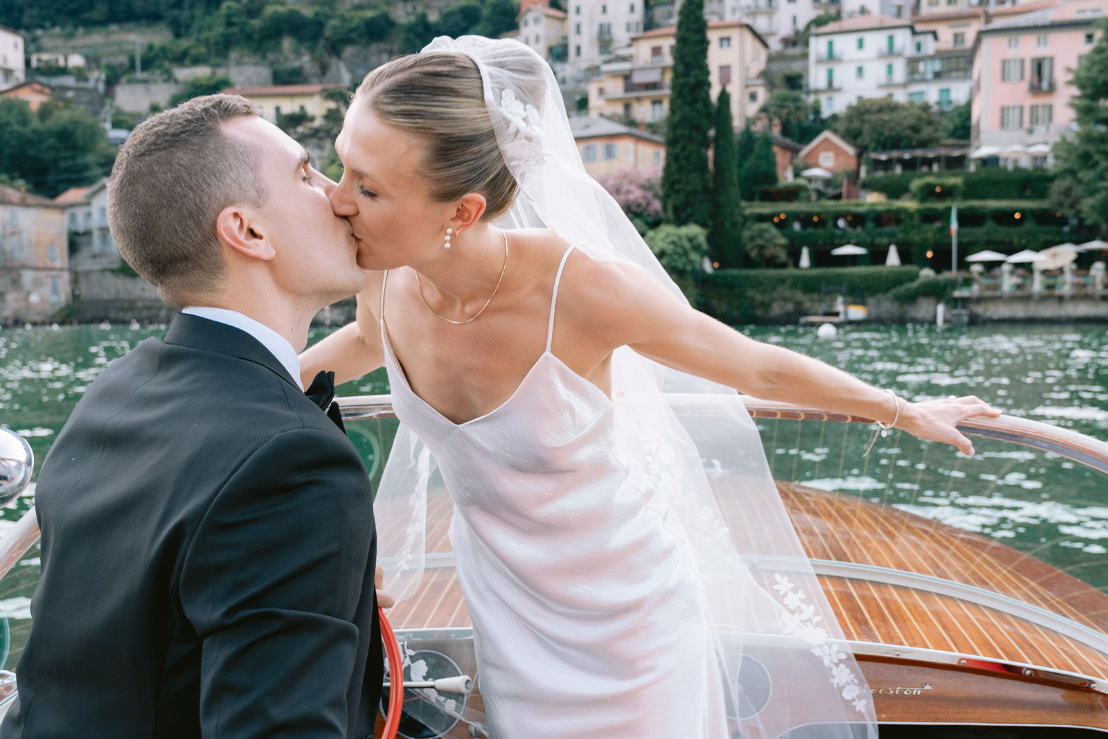 Bride and groom kissing on a boat near a scenic waterfront.