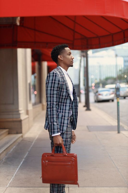 A man in a checkered suit holding a briefcase under a red canopy.