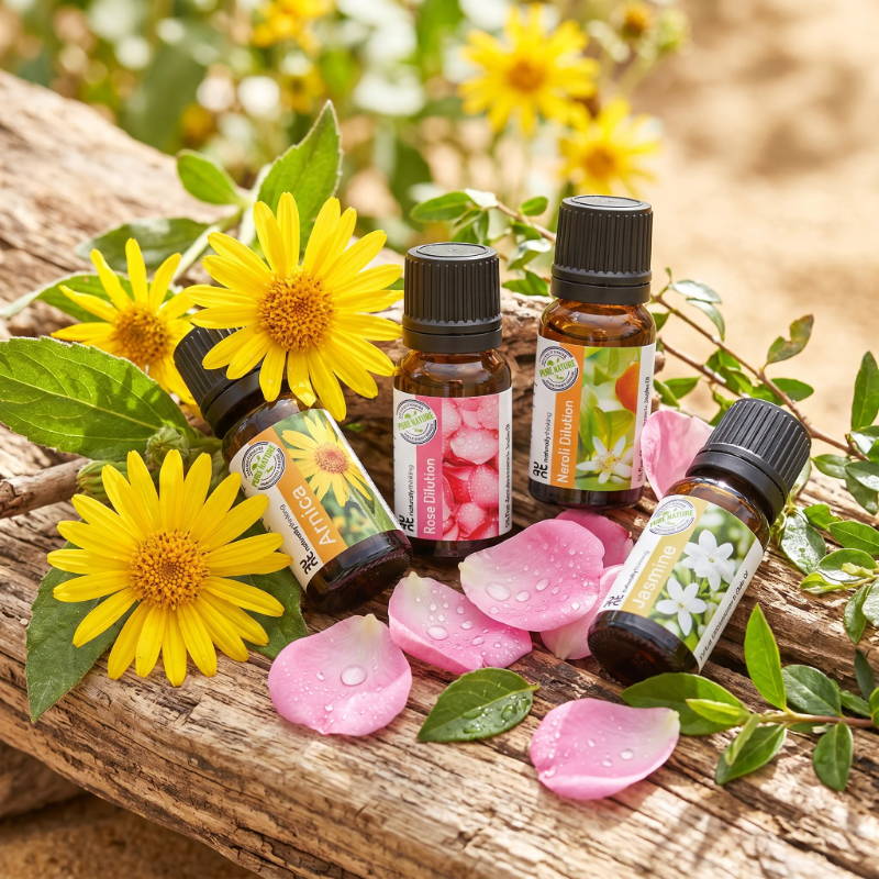 Bottles of essential oils surrounded by flowers and petals on a wooden surface.