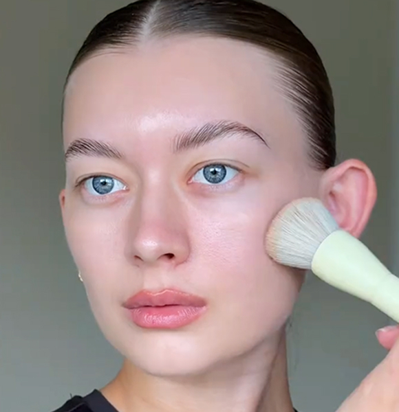 Person applying makeup with a brush on their cheek.