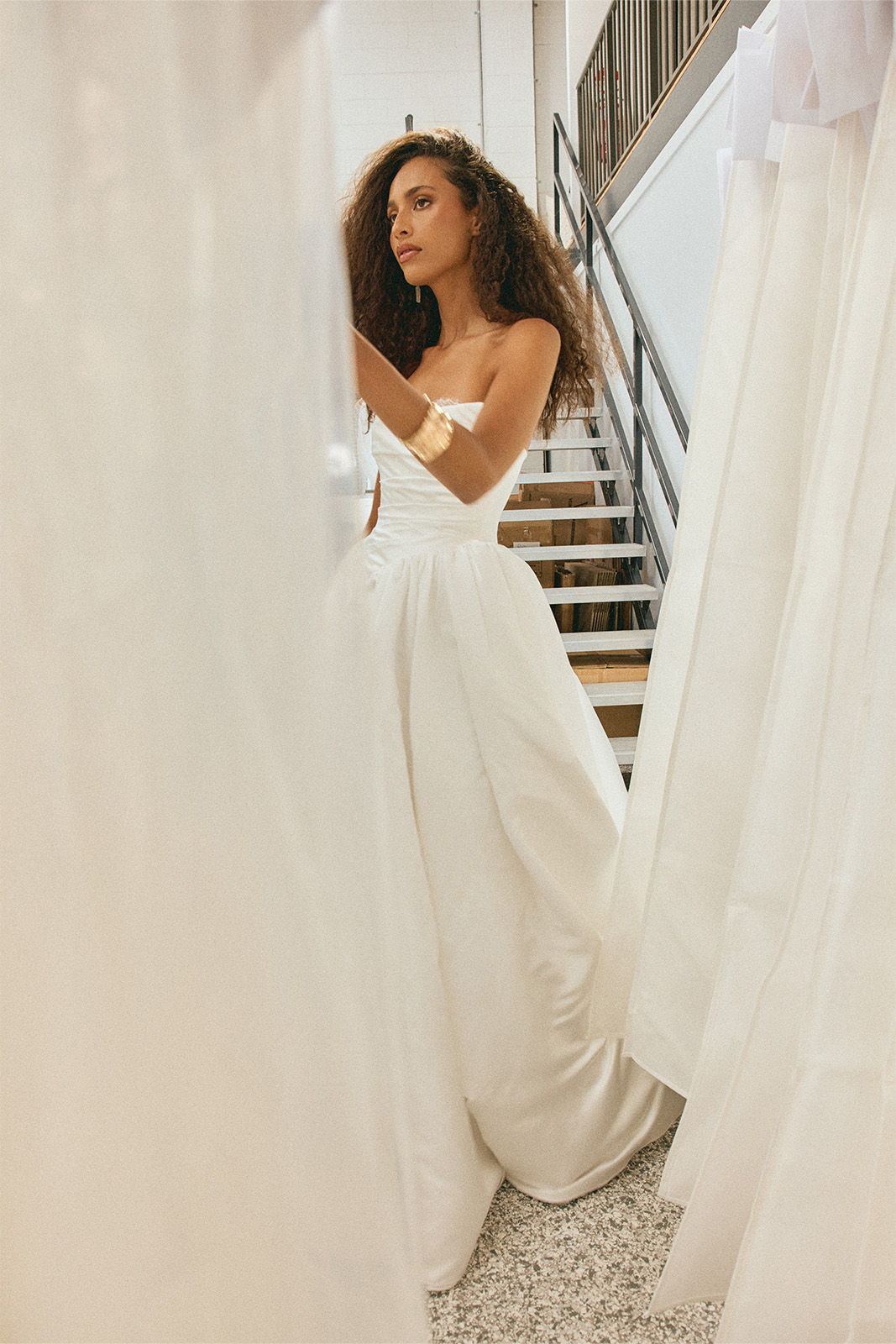 A woman in a white dress stands amidst white fabric drapes.