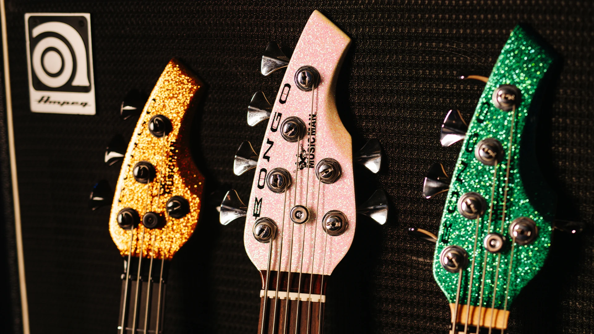 Three Music Man Bongo bass headstocks in various colours against a black background.