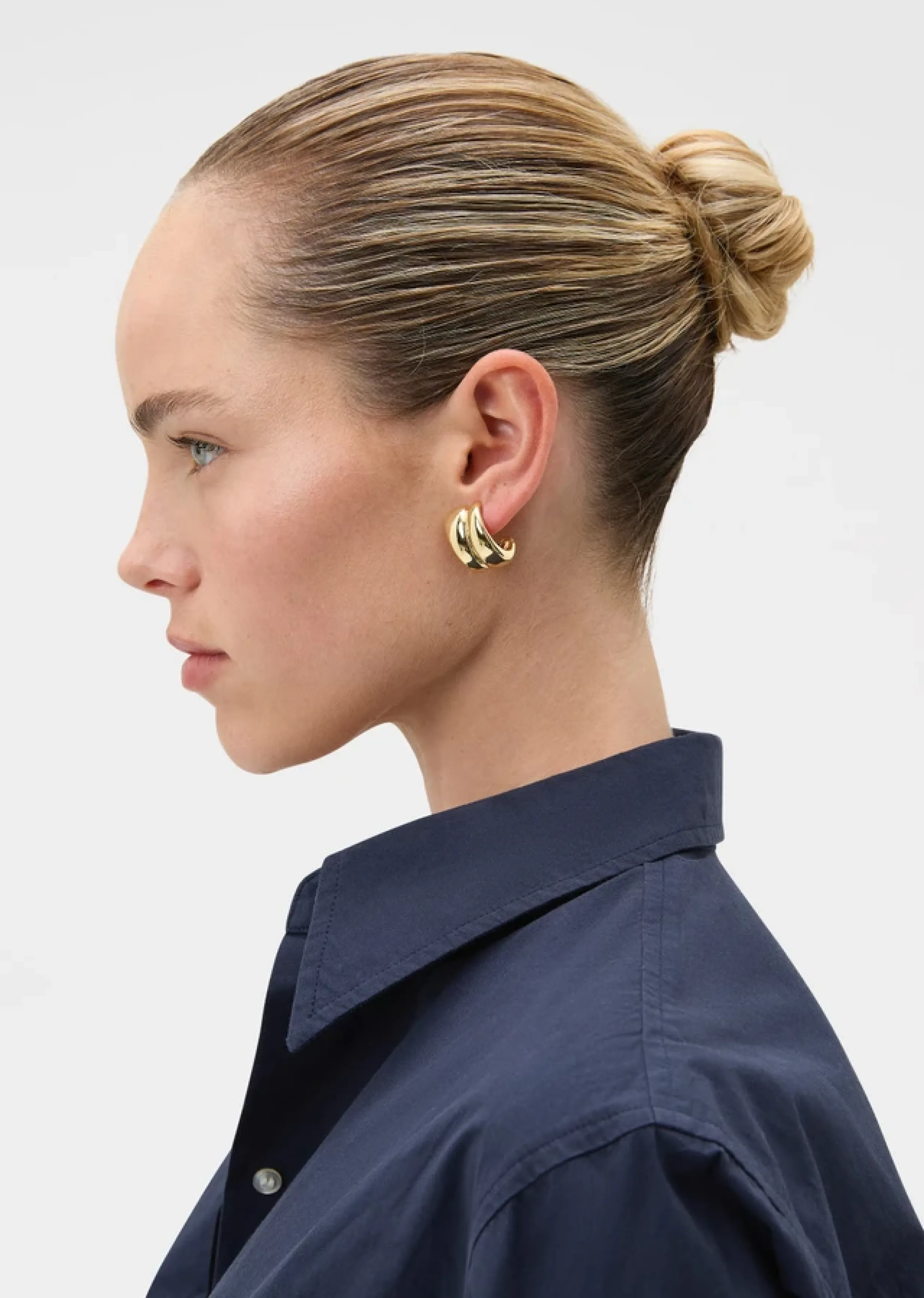 Profile view of a woman wearing a dark shirt and gold earrings.