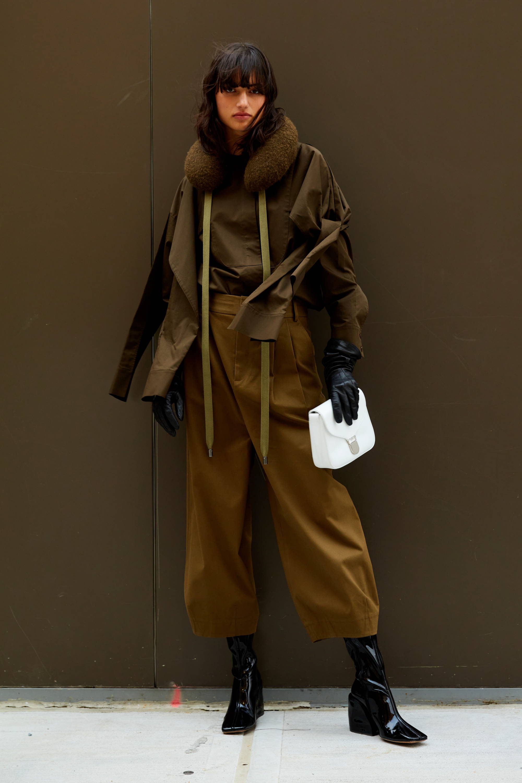 Model in stylish brown outfit with gloves and a white bag.